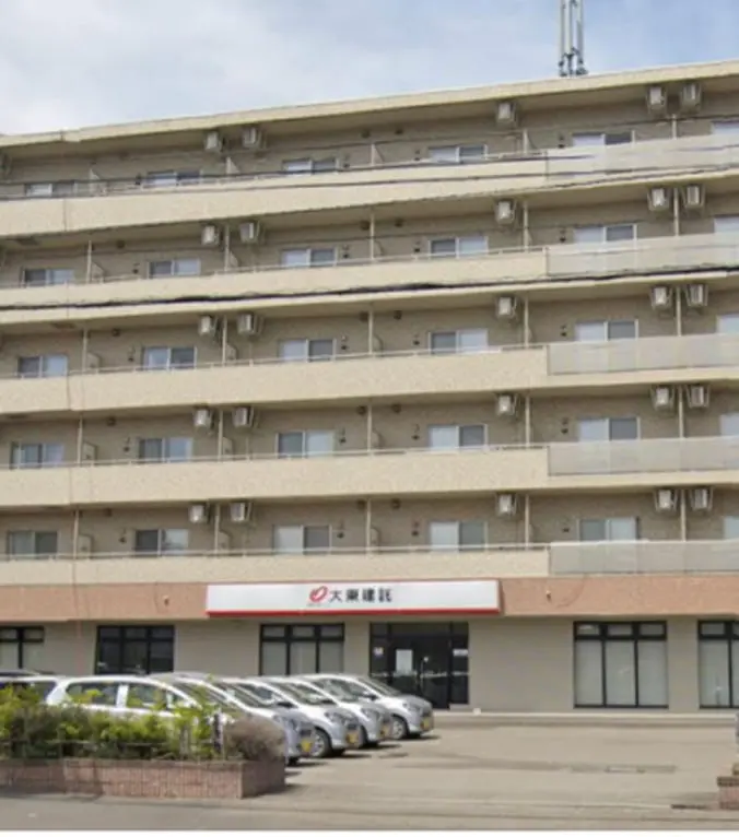 低層マンションの外観で、1階には企業の看板があり、建物前には社用車が多数駐車されている
                                                