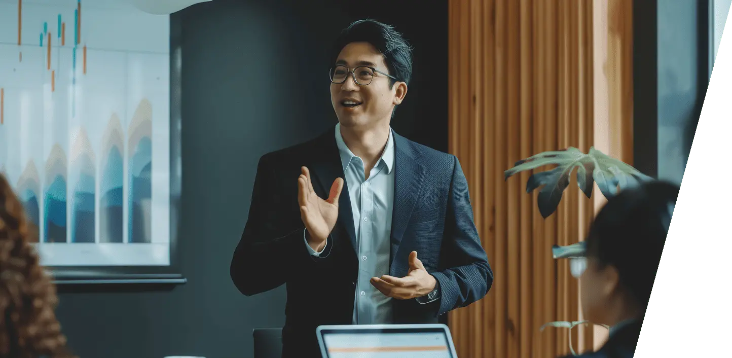 プレゼン中のスーツ姿の男性が話している場面で、オフィス内でのビジネスミーティングの一幕を表現