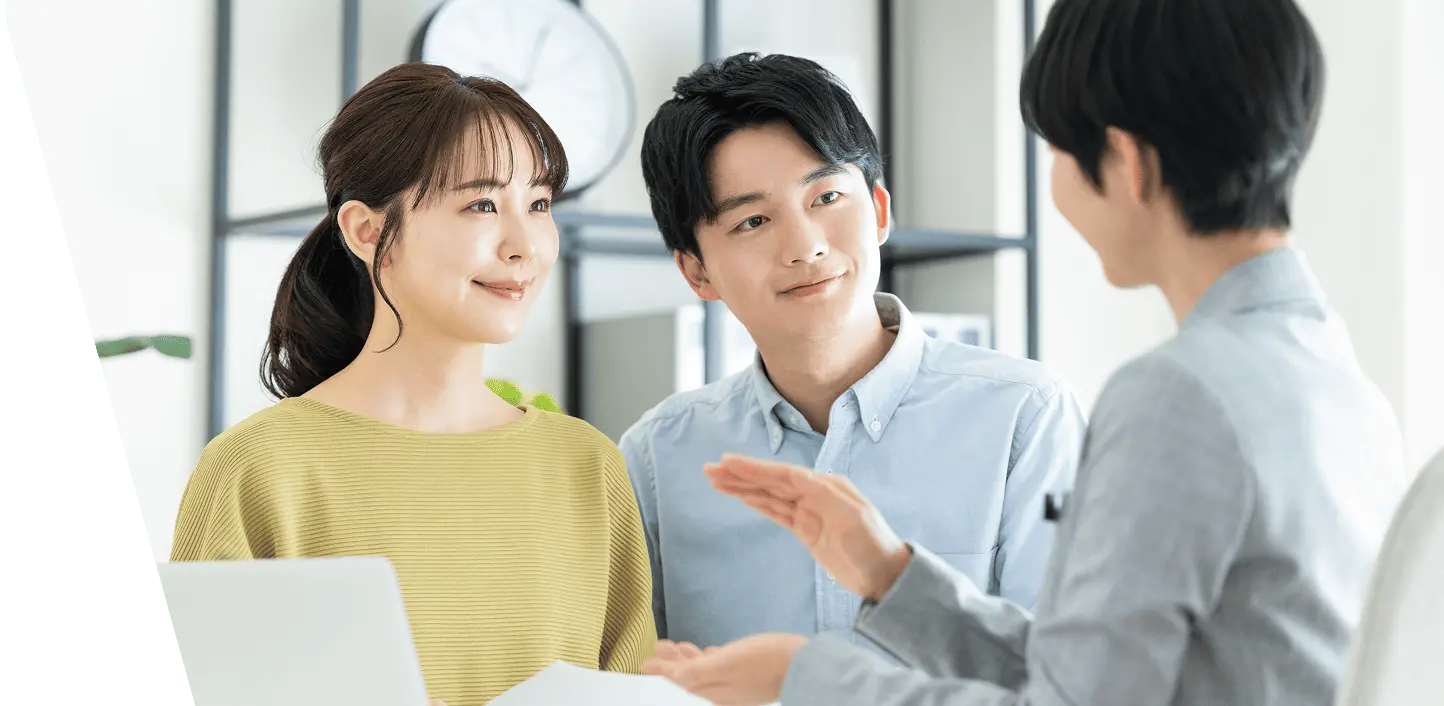不動産の相談風景を写した写真で、若い夫婦が営業担当者と穏やかな表情で会話している様子